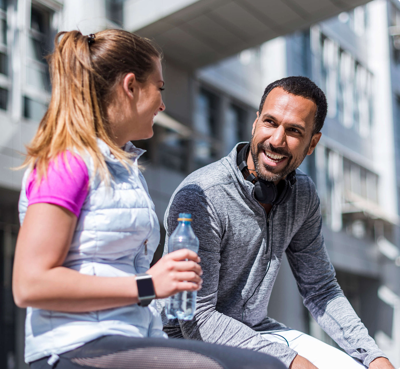 Two people sitting outdoors, one holding a water bottle, with a building in the background.