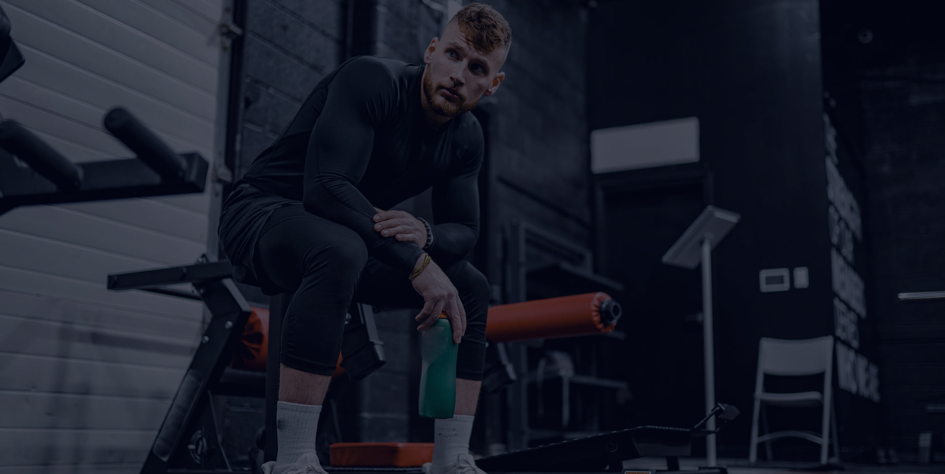 Person sitting on a bench in a gym setting with exercise equipment.