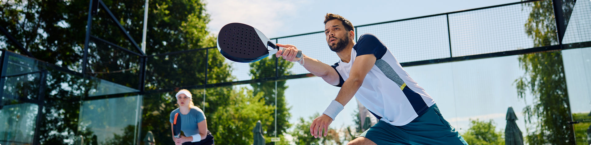 Man playing padel tennis with another player in a park setting