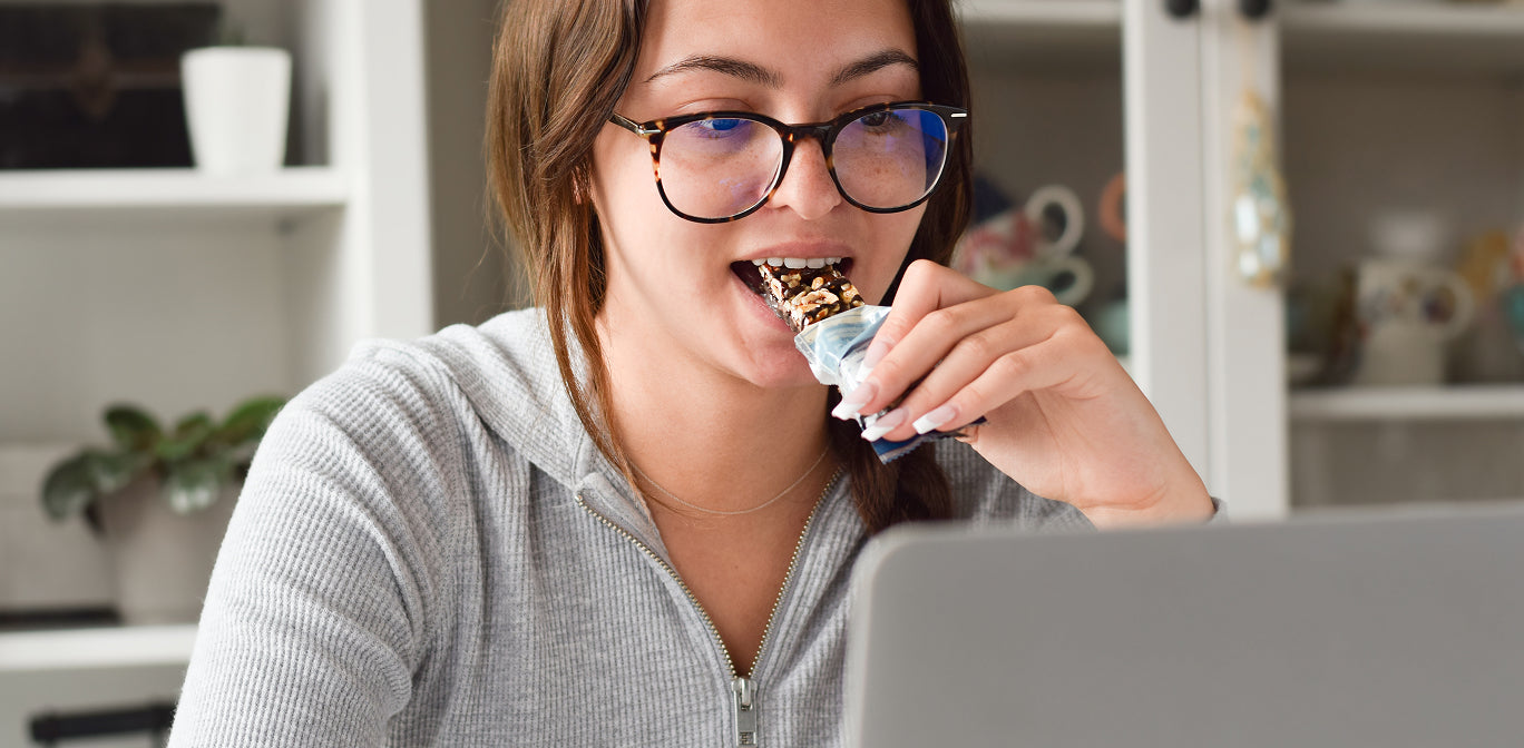Person eating a snack while using a laptop in a home setting